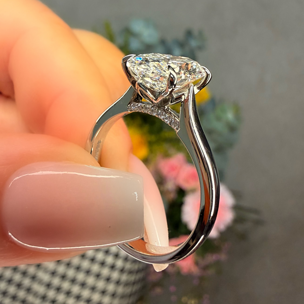 Diamond ring held by a hand with a blurred floral background