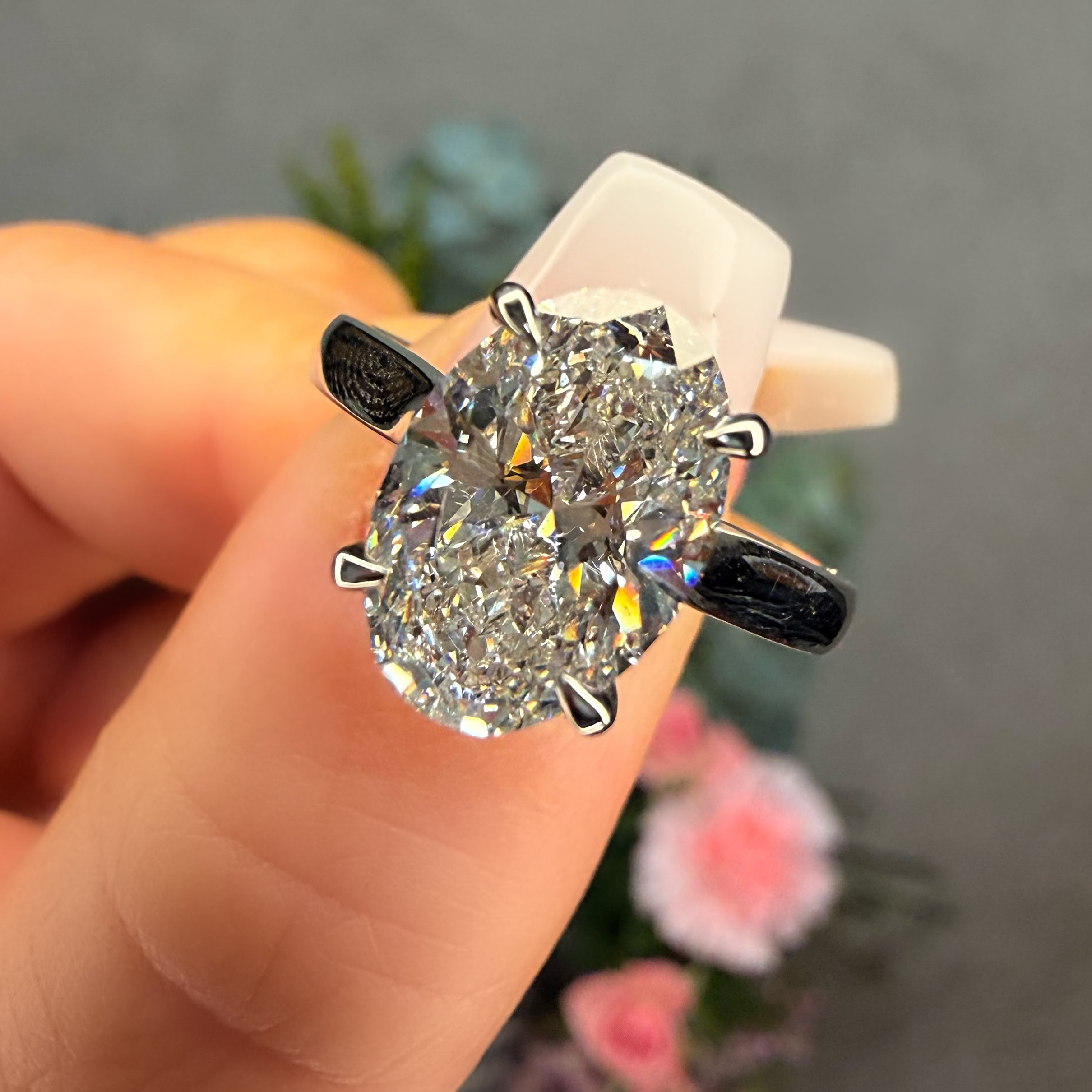 Diamond ring held in a hand with a blurred floral background