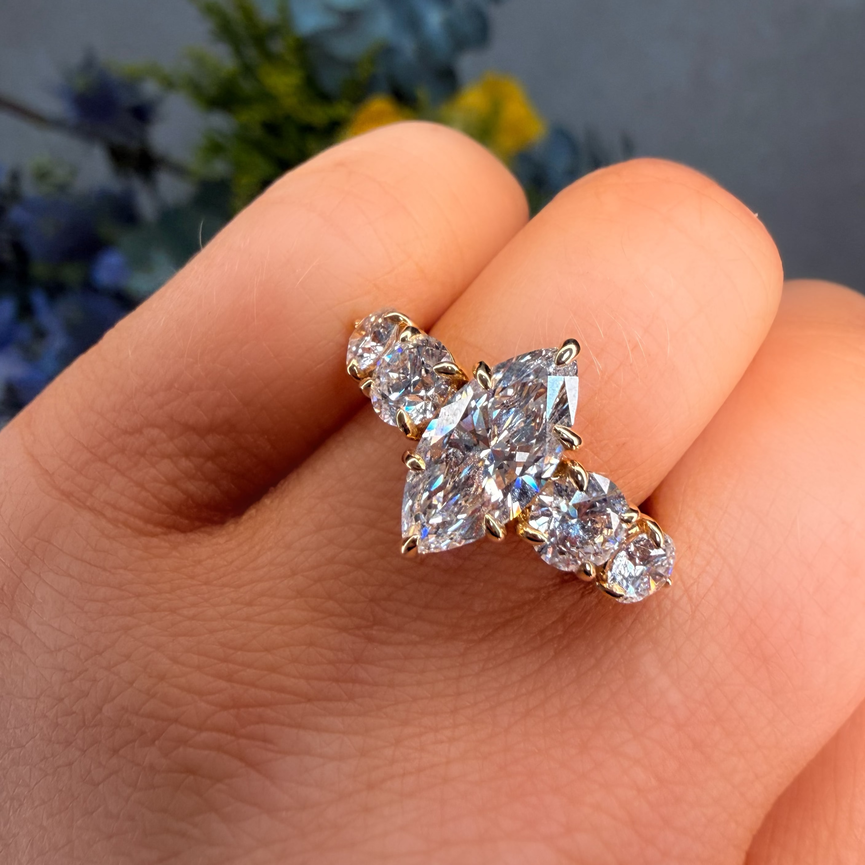 Diamond earrings held between fingers with a blurred floral background