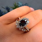 Ring with a dark gemstone and diamond accents on a hand against a blurred background