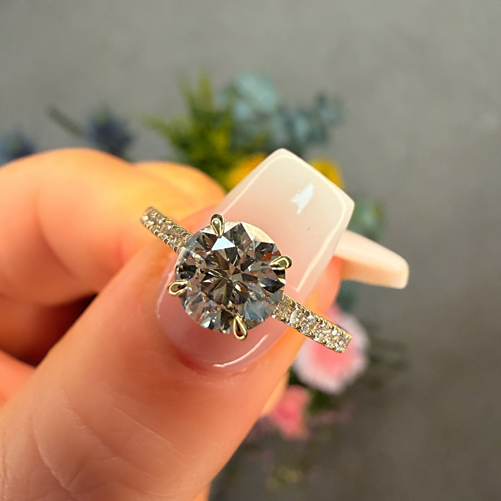 Diamond ring held between fingers with a blurred floral background