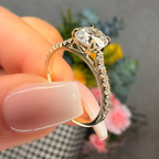Gold ring with a large diamond held by a hand against a blurred floral background
