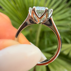 Silver ring with a large diamond held between fingers against a green leafy background
