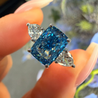 Blue gemstone ring held by a hand with a blurred natural background