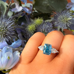 Blue gemstone ring on a hand with flowers in the background