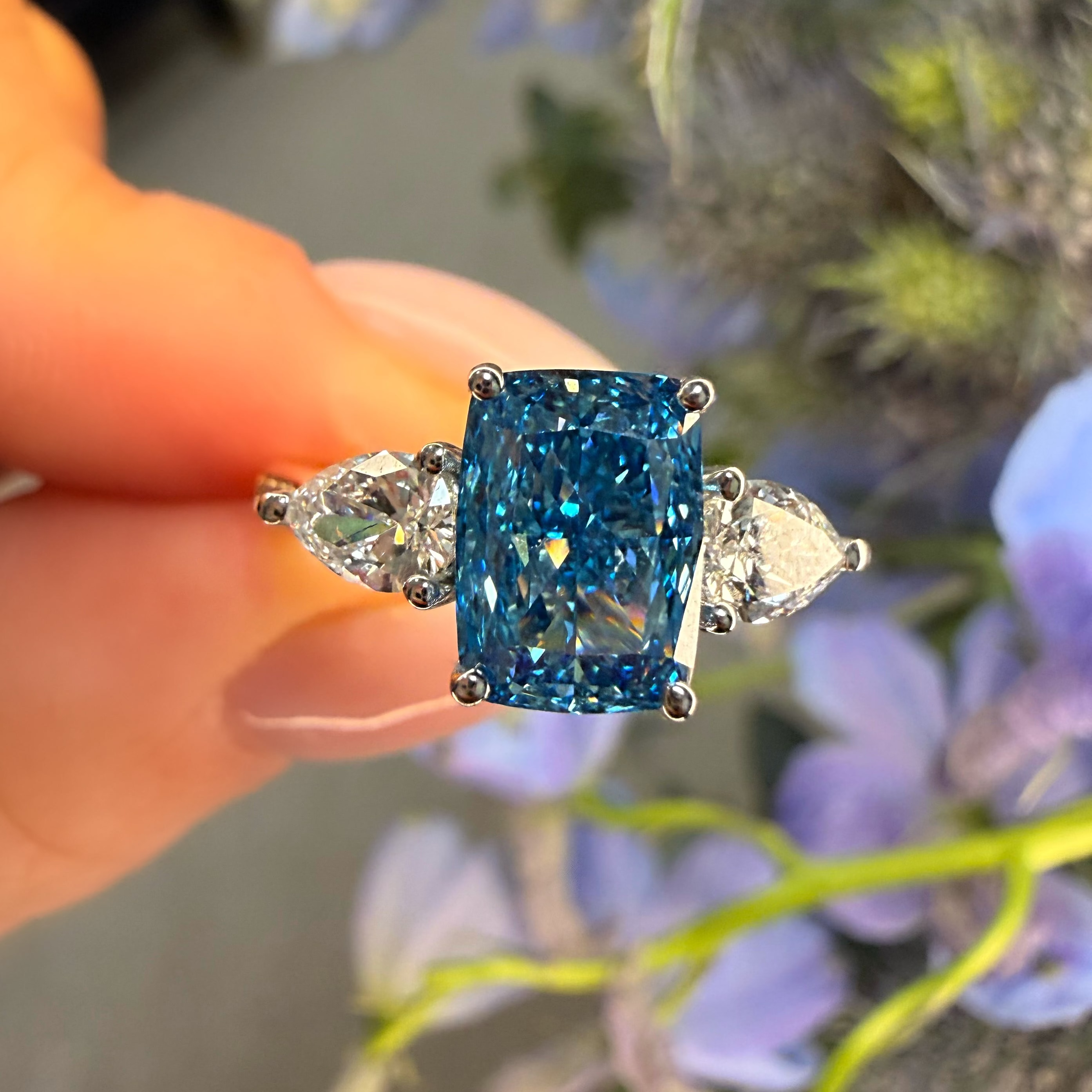 Blue gemstone ring held by a hand with a floral background