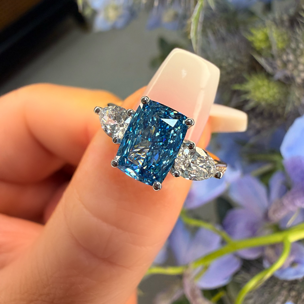 Blue gemstone earring held by a hand with a floral background