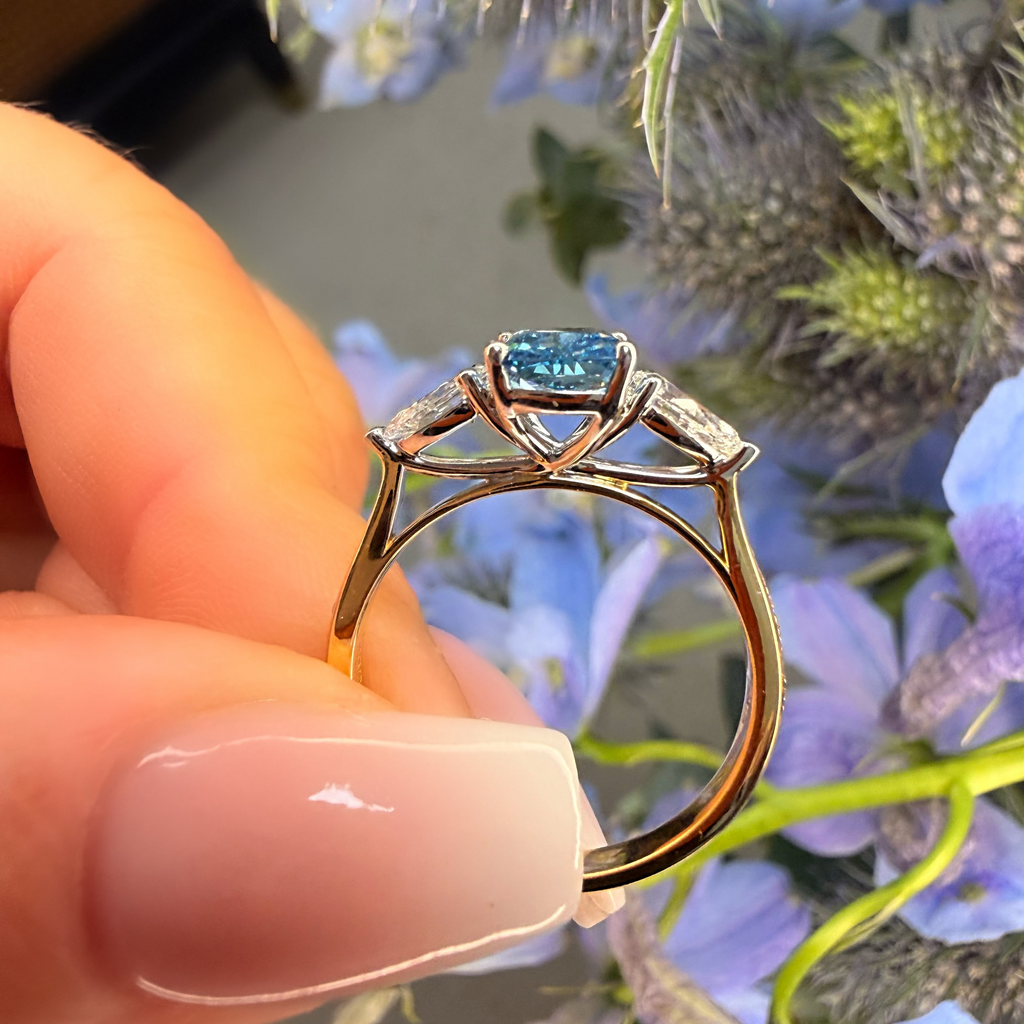 Gold ring with a blue gemstone held by a hand in front of flowers
