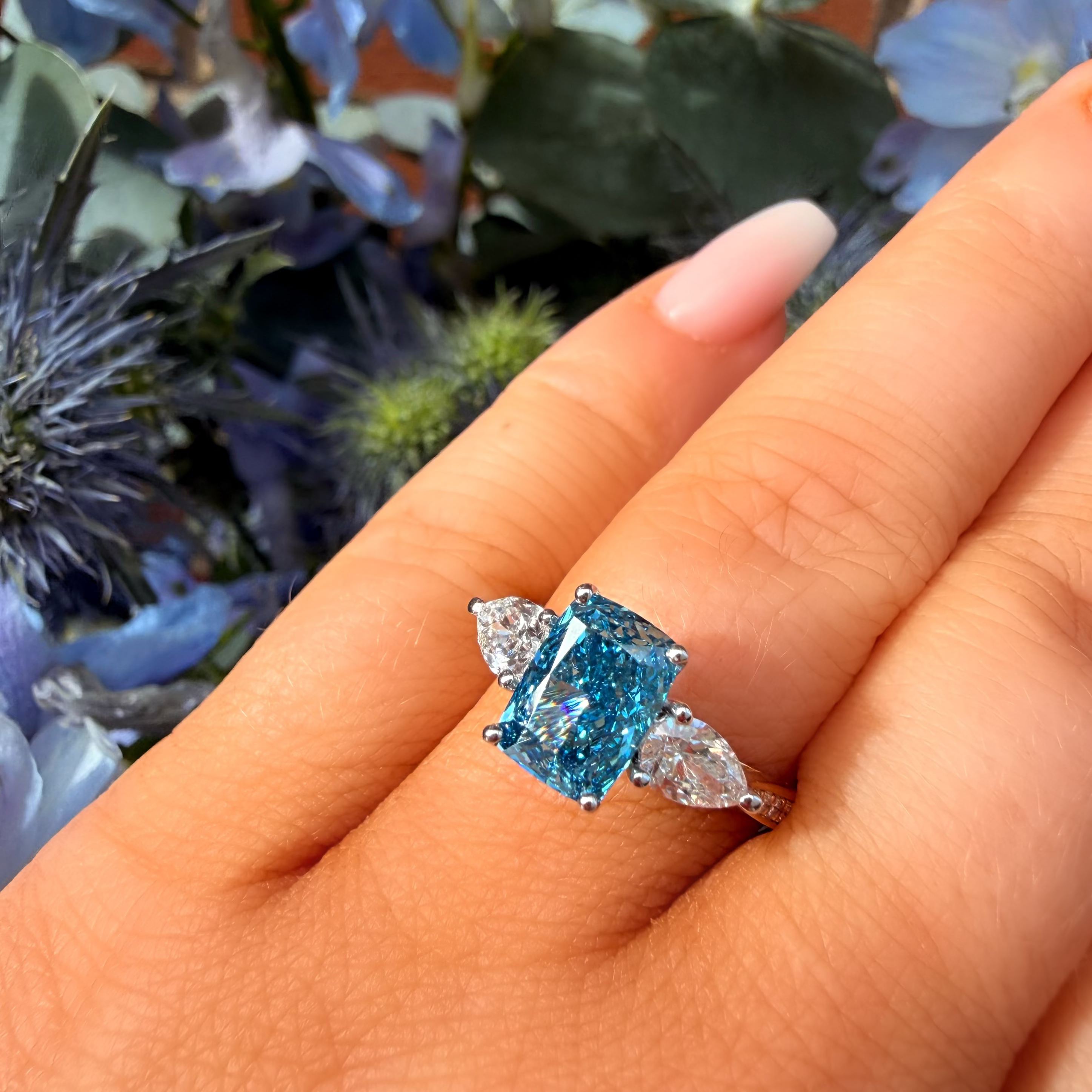 Blue gemstone ring on a hand with flowers in the background