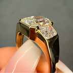 Gold and black diamond ring held by a hand against a gray background