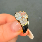 Gold and black ring with diamonds held by a hand against a dark background