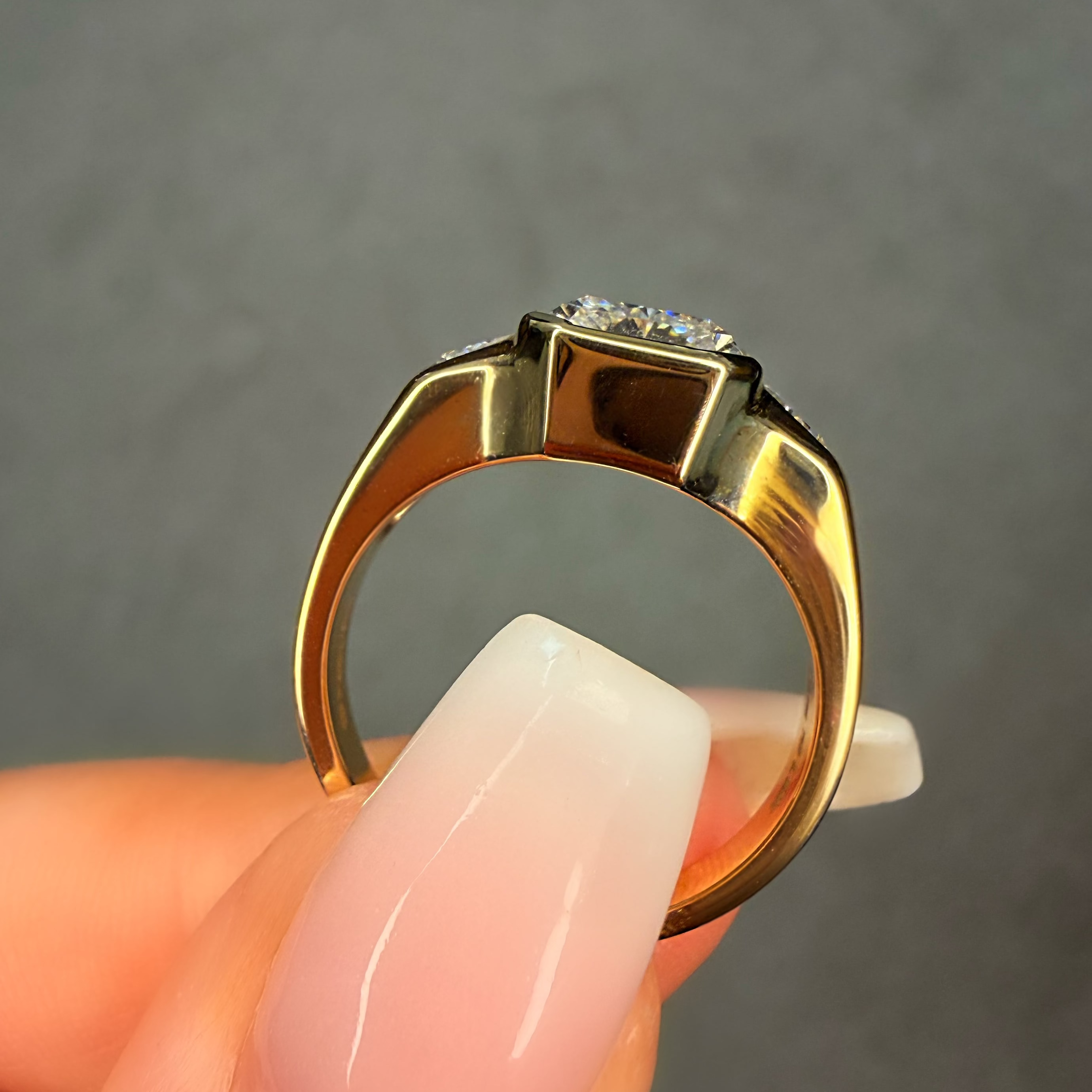 Gold ring with a diamond held between fingers against a gray background