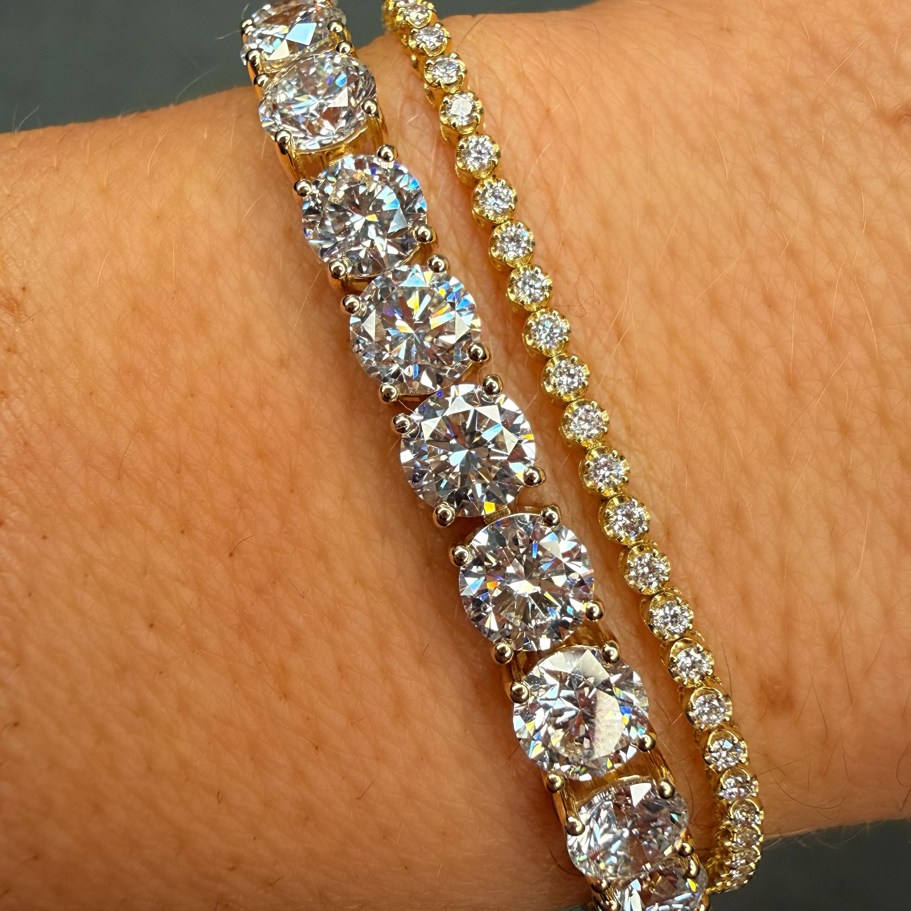 Two diamond bracelets on a wrist against a neutral background