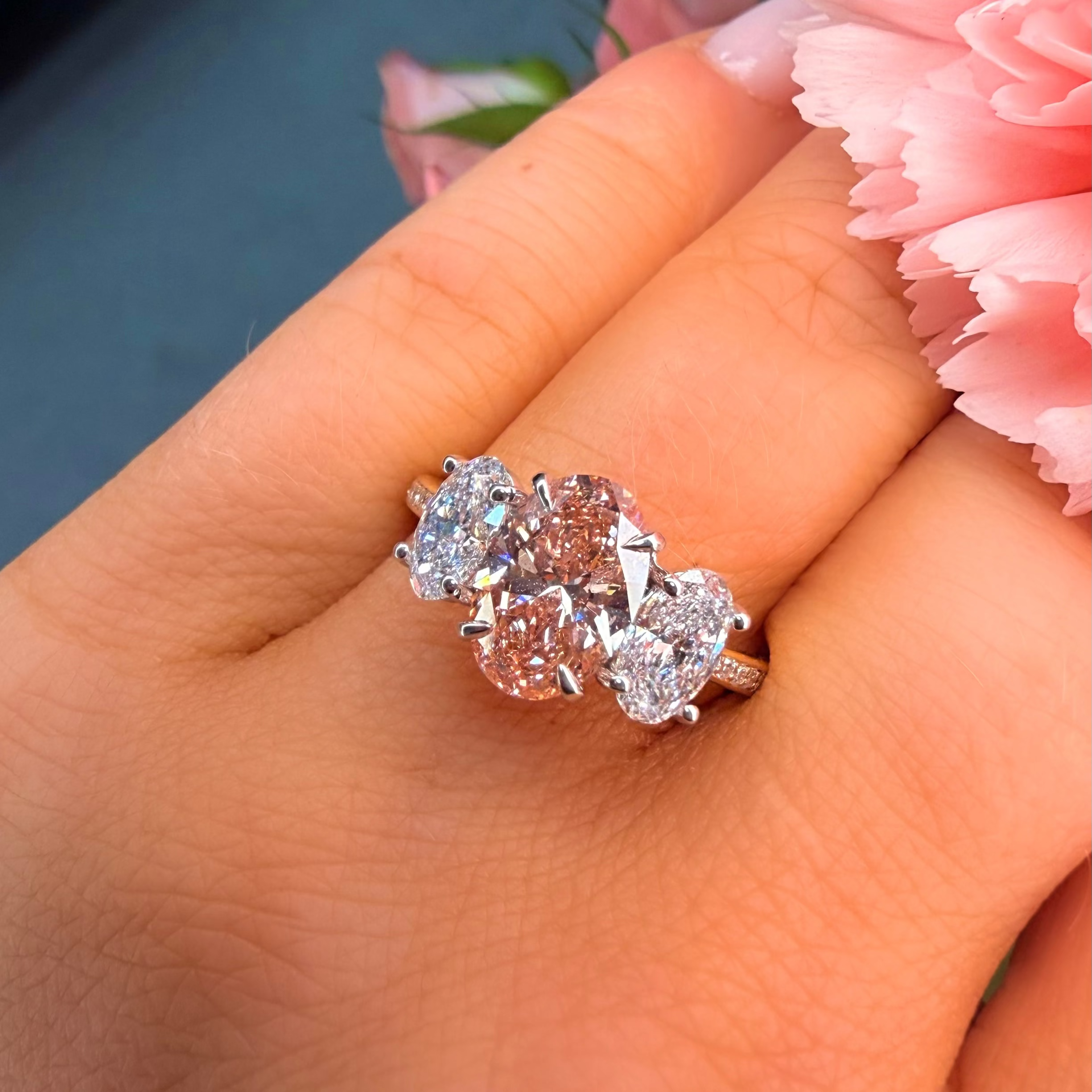Ring with three diamonds on a hand with pink flowers in the background