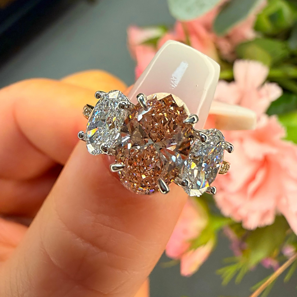Diamond ring held in a hand with flowers in the background