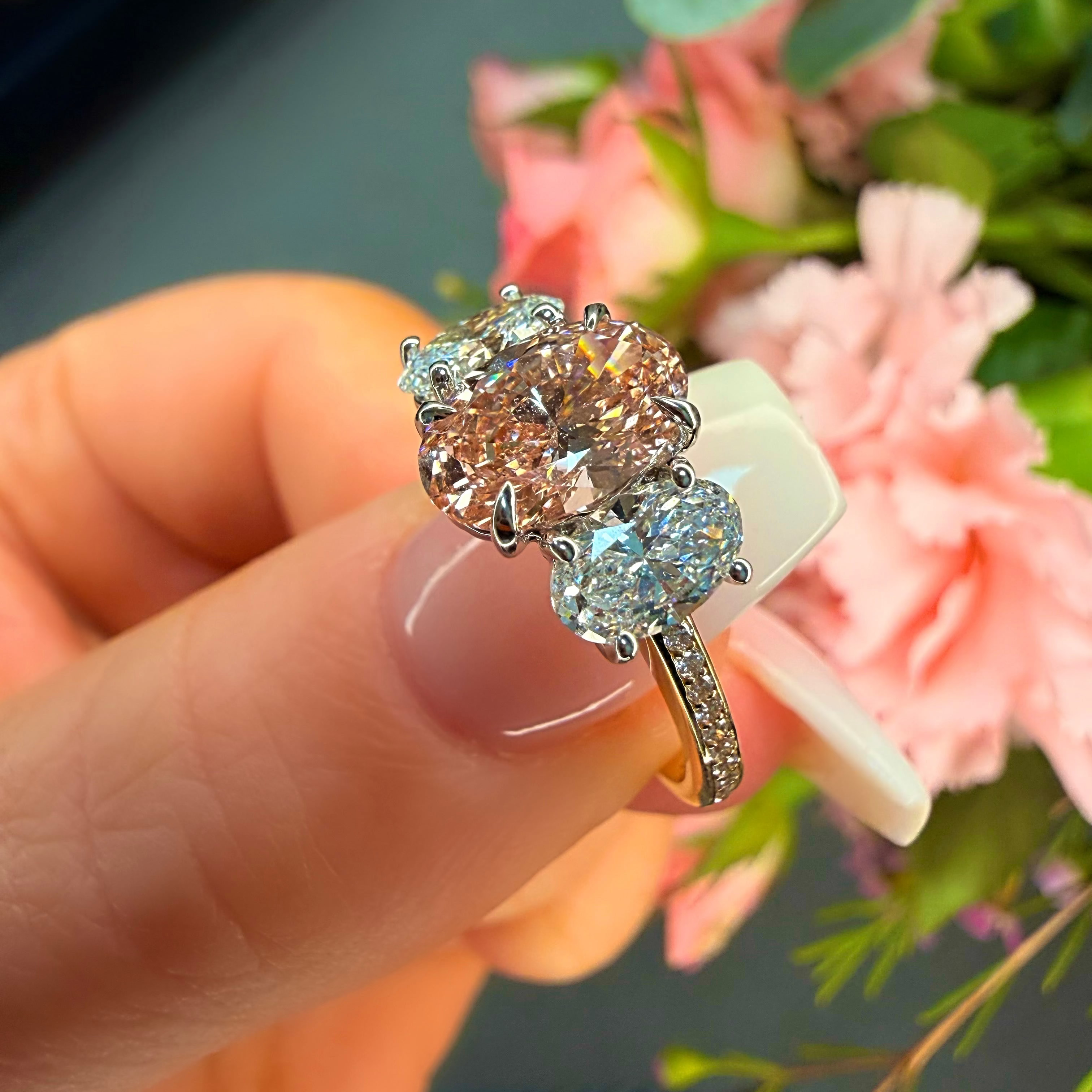 Silver ring with a large central gemstone and smaller stones on a hand with flowers in the background