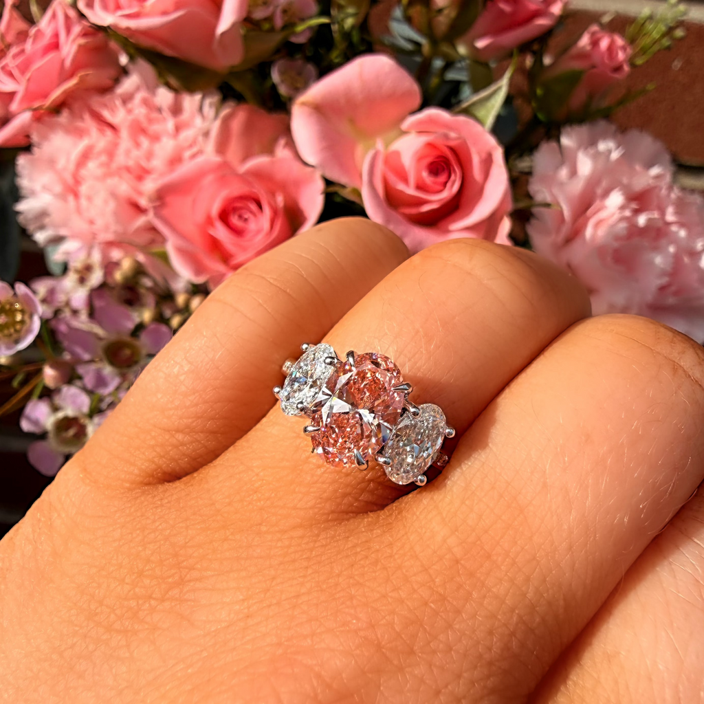 Ring with pink gemstone on a finger in front of pink flowers