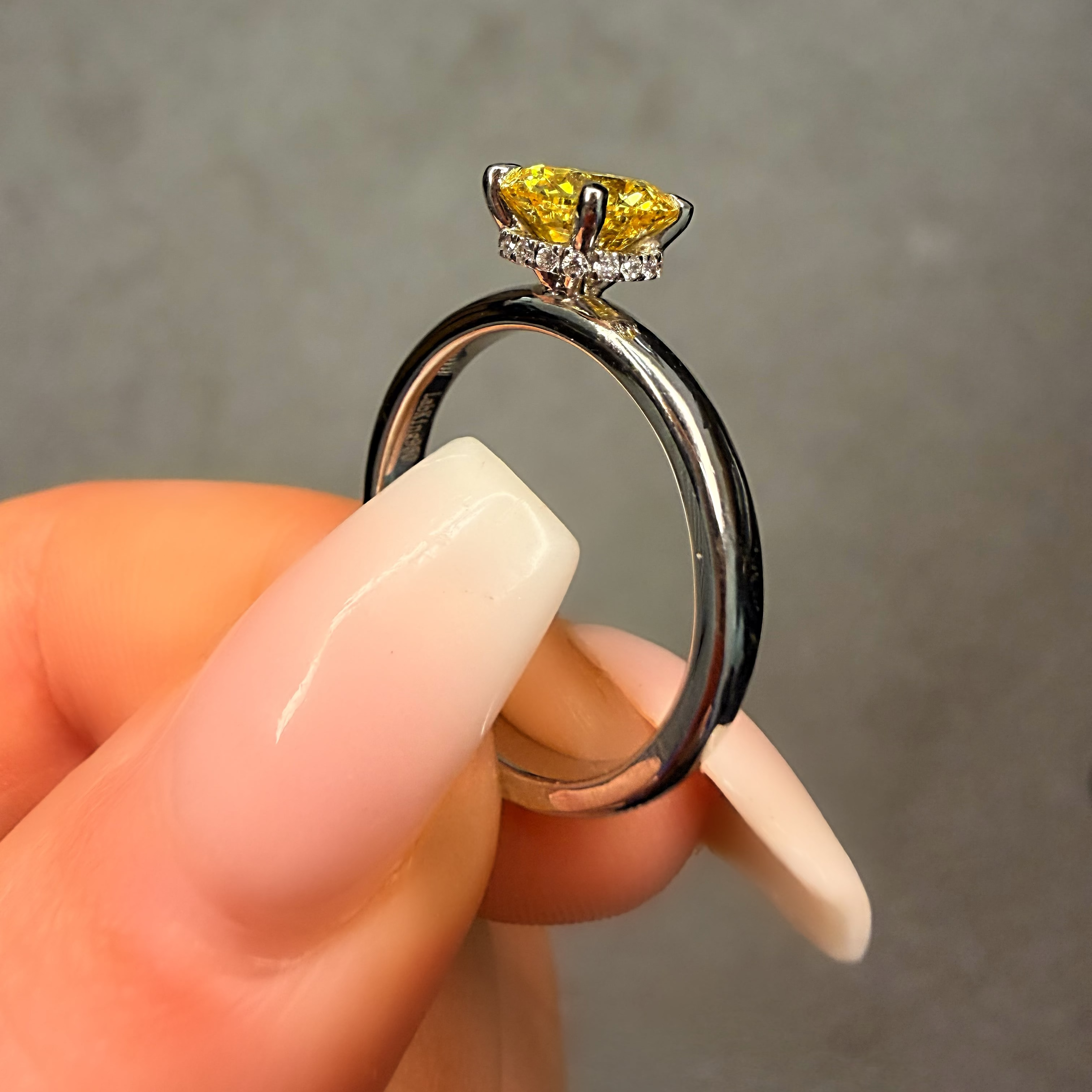 Silver ring with a yellow gemstone held by a hand against a neutral background