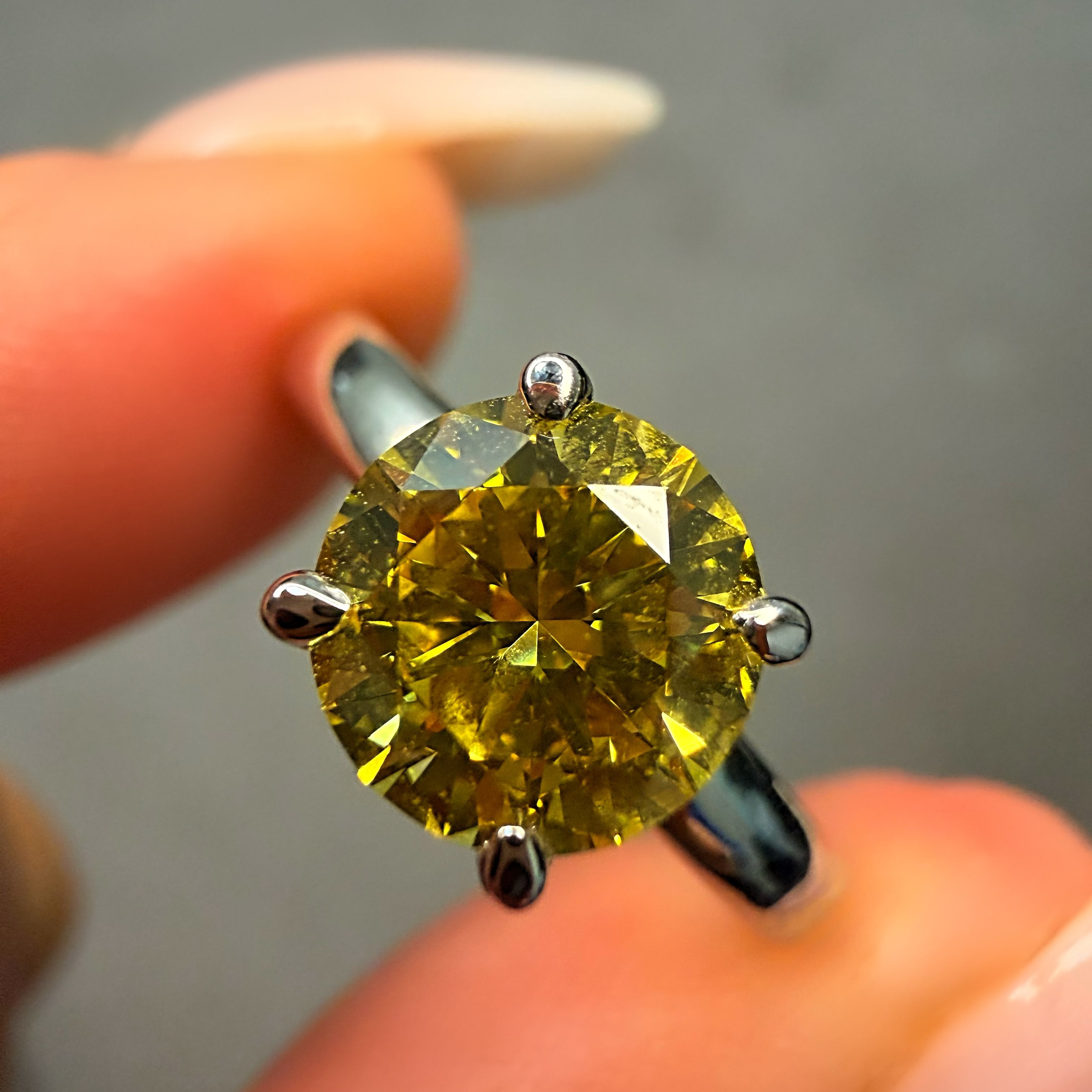Yellow diamond ring held between fingers with a blurred background