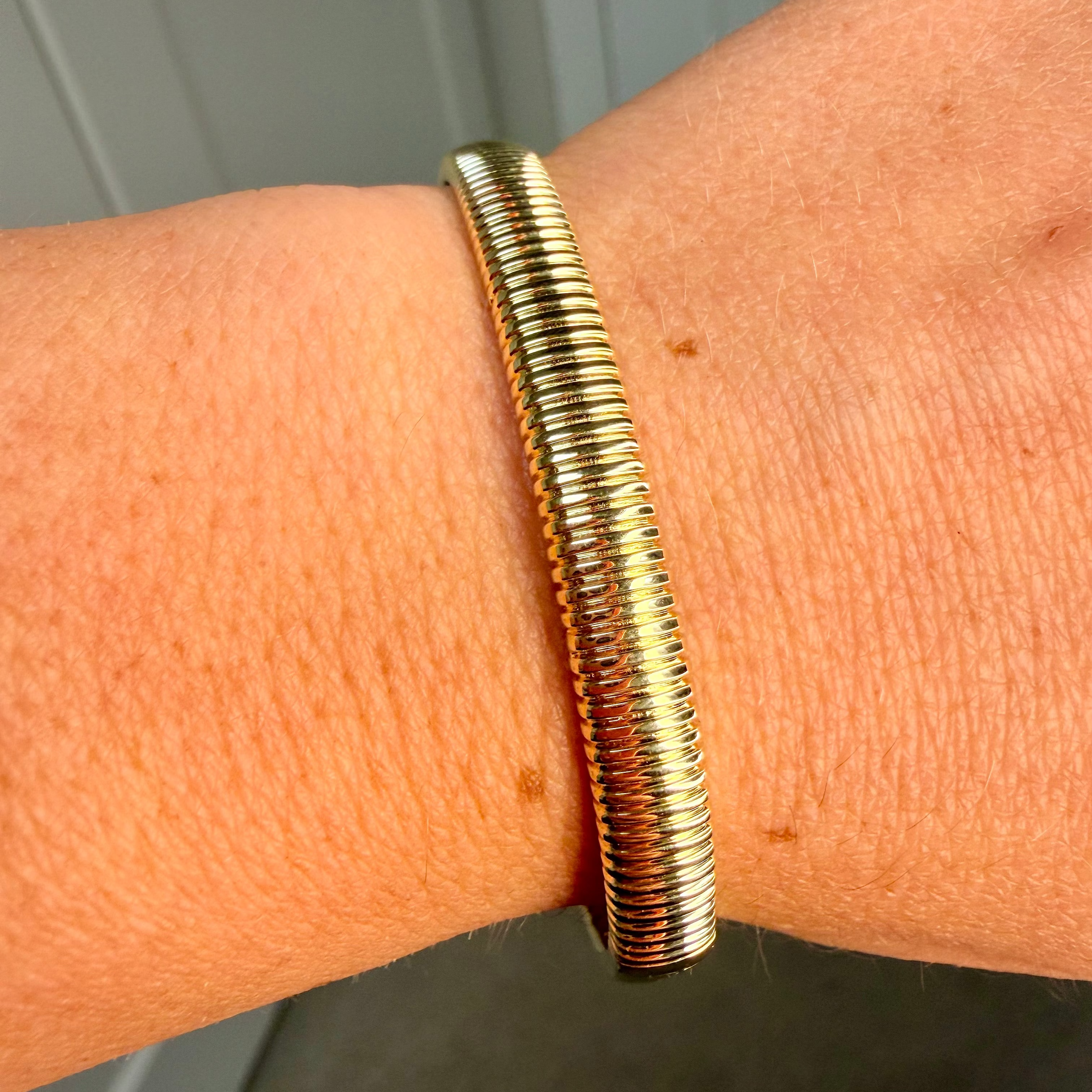 Gold bracelet on a wrist with a neutral background