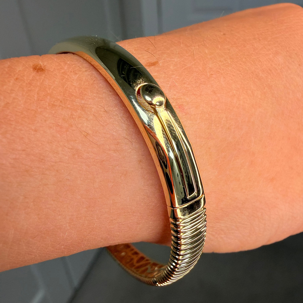 Gold bracelet on a wrist with a neutral background