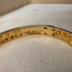 Gold bracelet with intricate design on a beige cushion