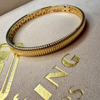 Gold bracelet on a beige surface with 'Buccellati' branding.