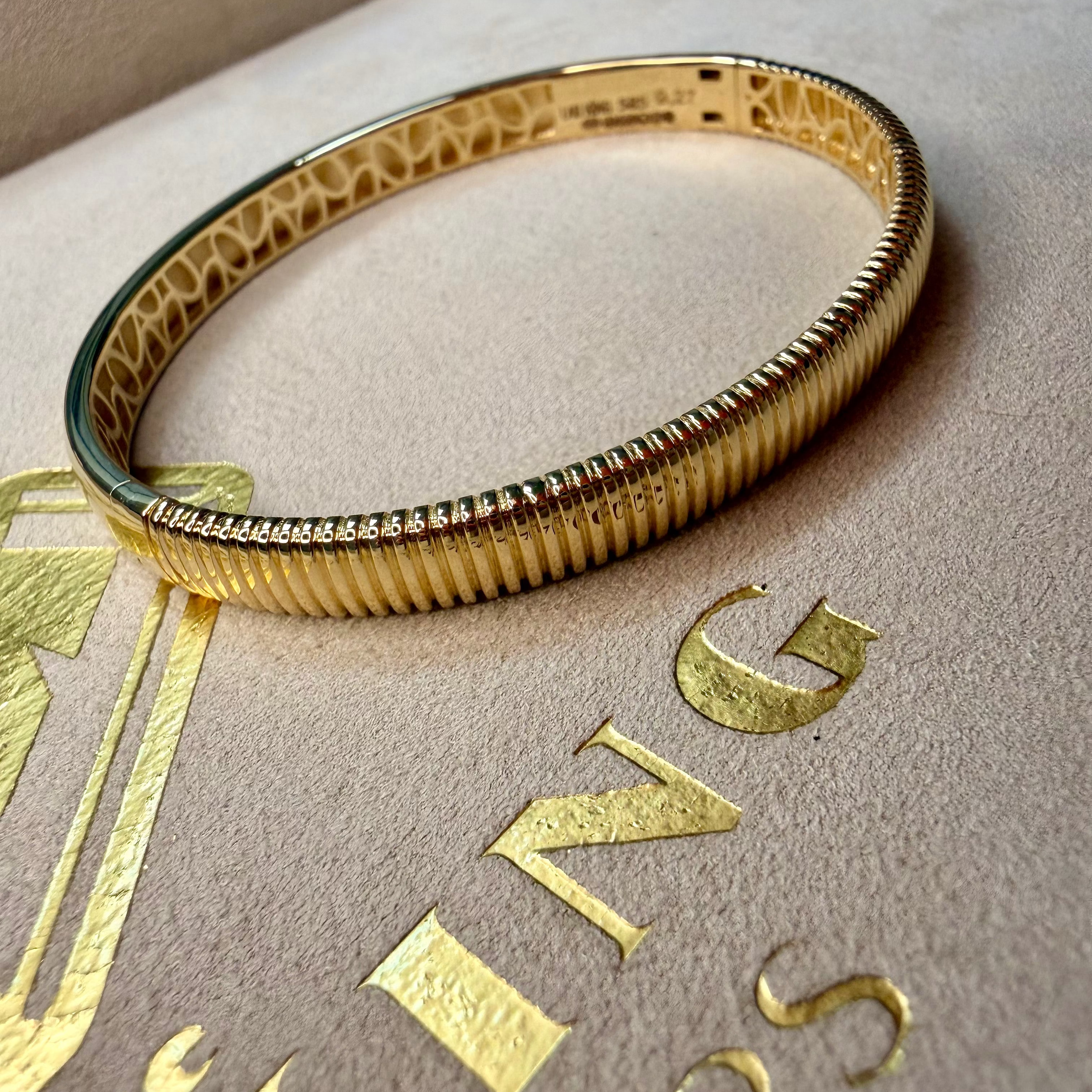 Gold bracelet on a beige surface with 'Buccellati' branding.