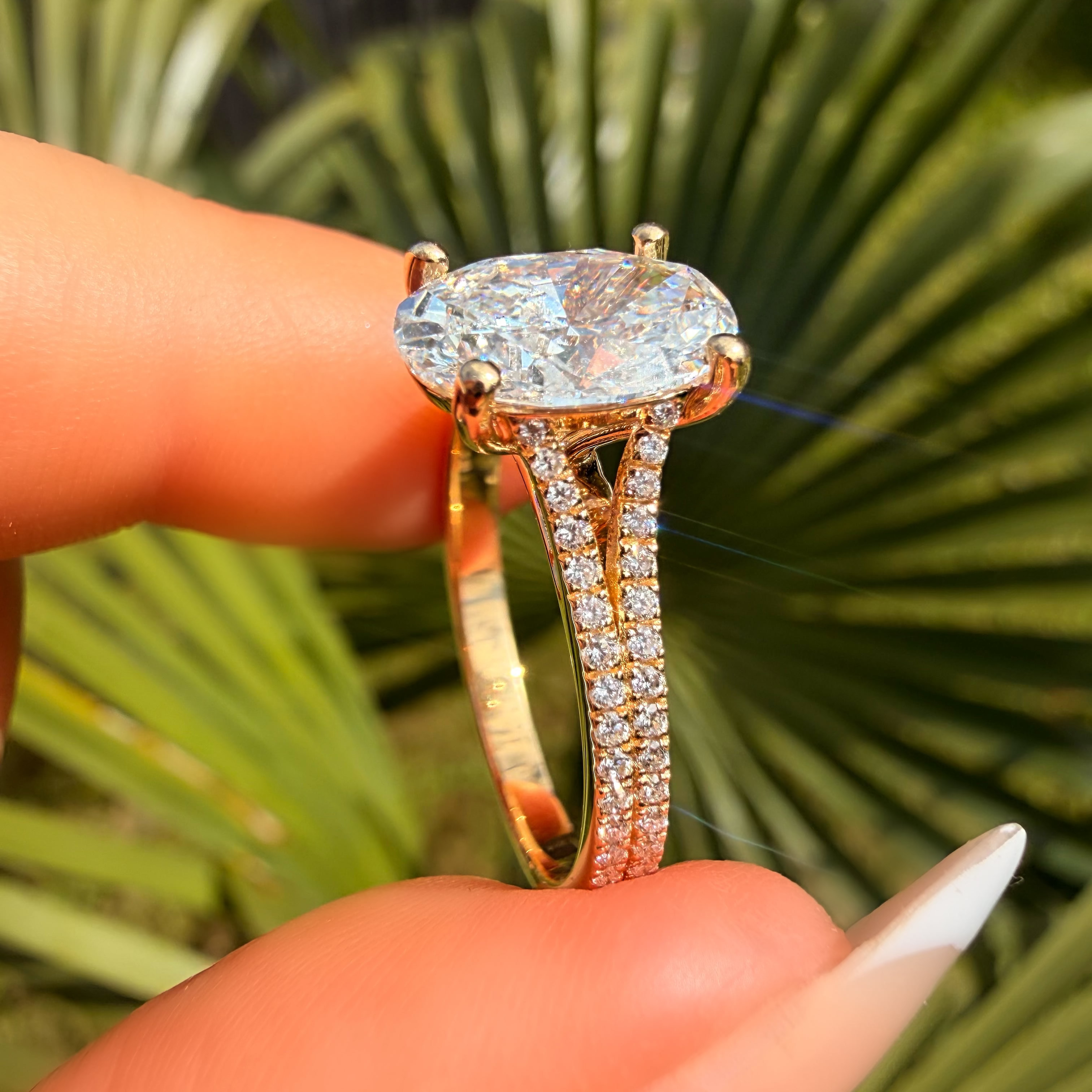 Rose gold ring with a large diamond held by a hand against a green leafy background