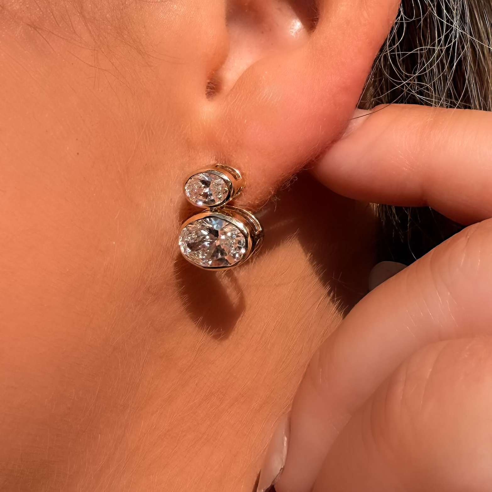 Close-up of a person wearing gold earrings with clear stones.