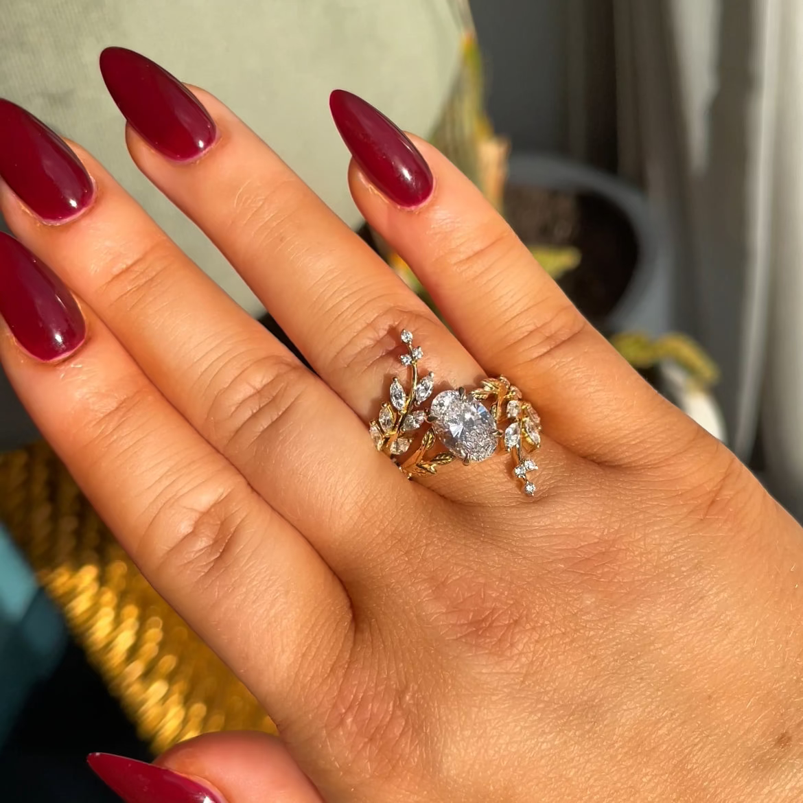 Hand wearing a ring with a large diamond, set against a blurred indoor background.