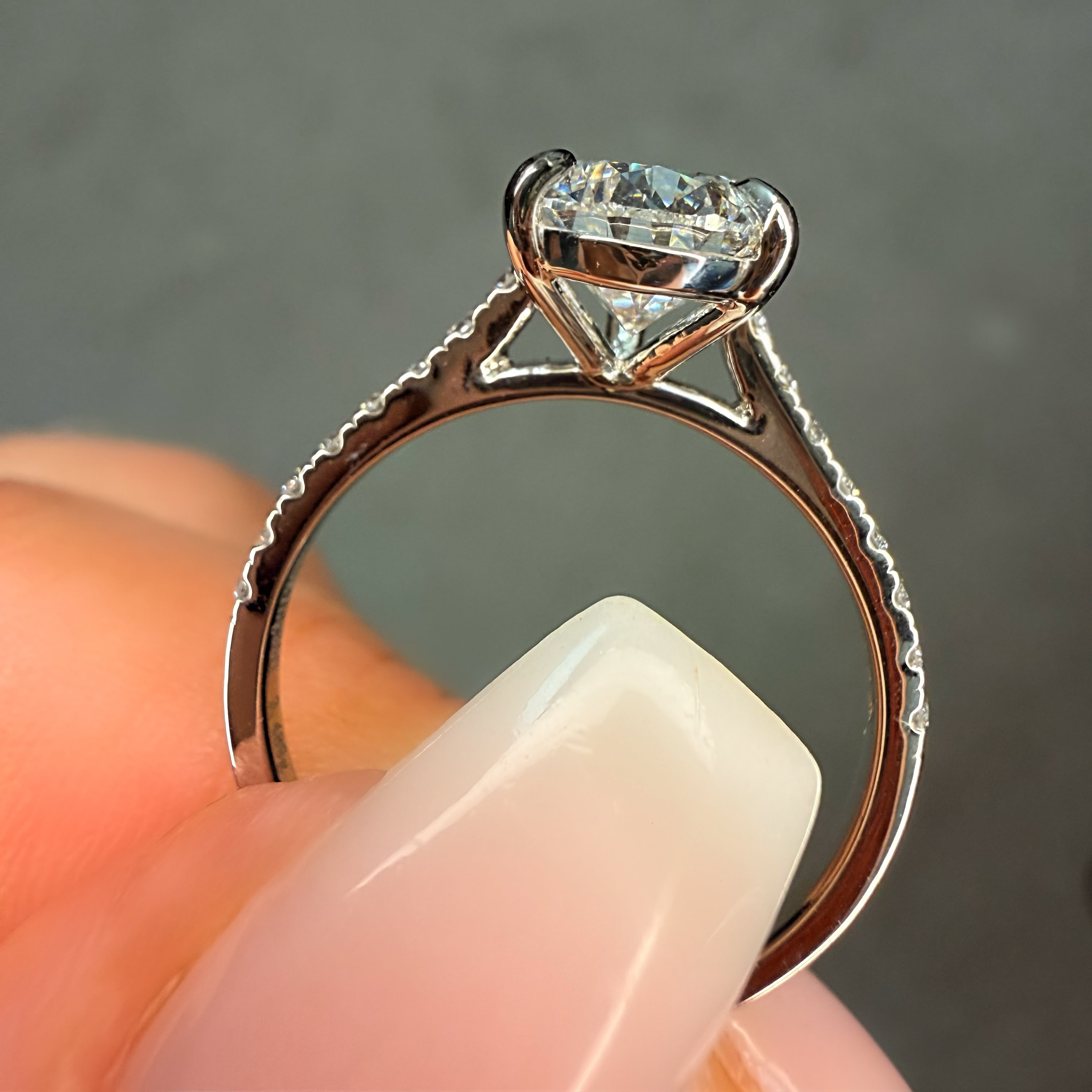 Rose gold ring with a diamond held between fingers against a neutral background