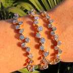 Two gold bracelets with clear stones on a wrist against a natural background