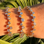 Gold bracelet with clear stones on a wrist against a green leafy background