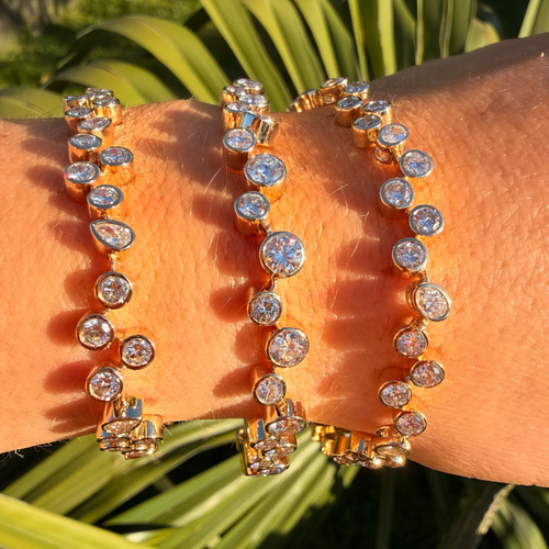 Gold bracelet with clear stones on a wrist against a green leafy background