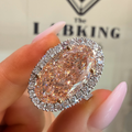 A close-up of a hand with pink manicured nails holding a large pear-shaped pink diamond ring with a halo of small clear stones. The background shows a blurred beige surface with the brand name 'The Labking' visible.