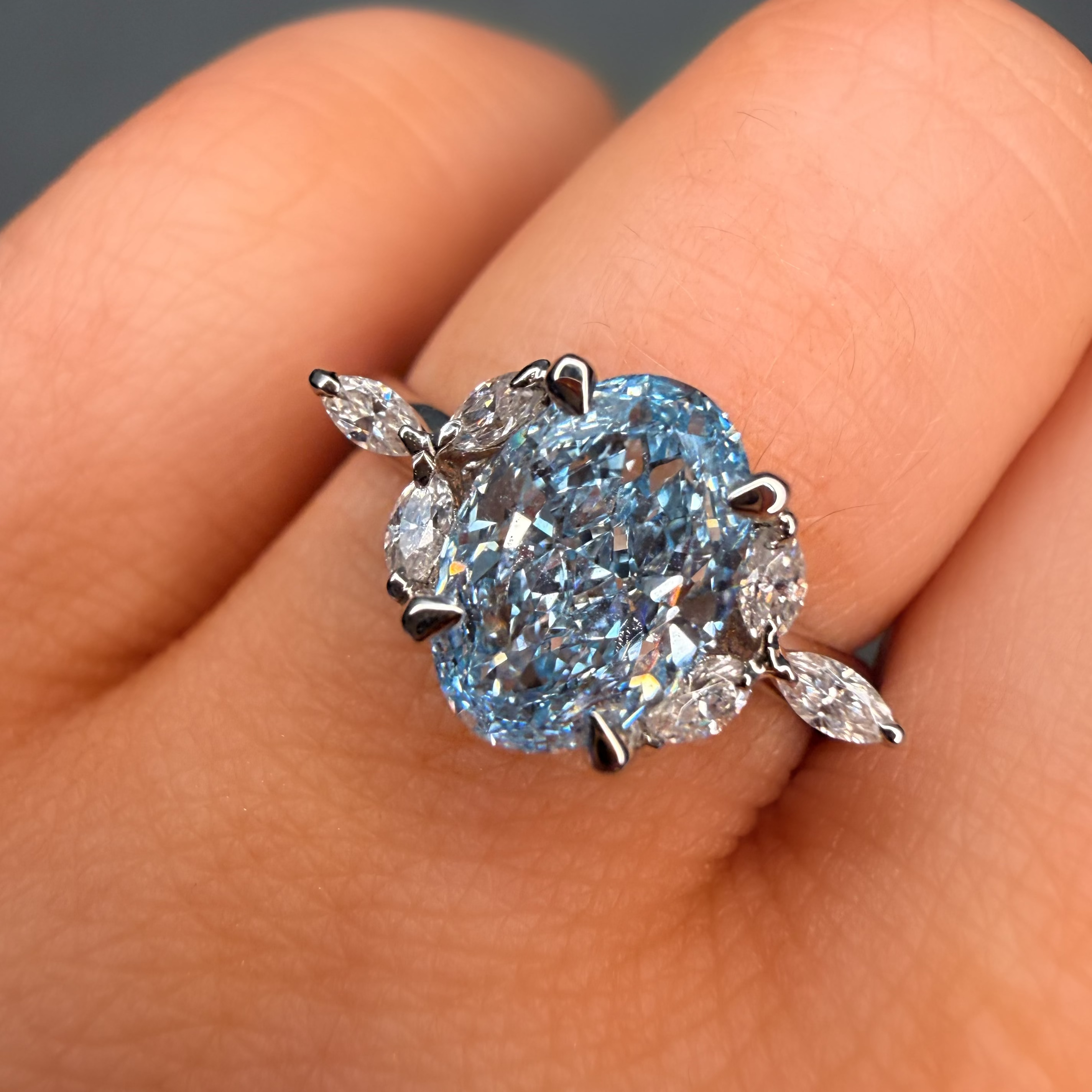 Blue diamond ring held between fingers against a neutral background