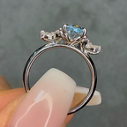 Silver ring with a blue gemstone held between fingers against a gray background