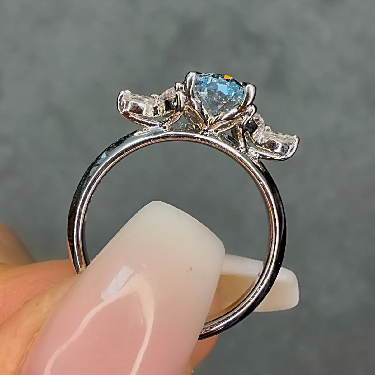Silver ring with a blue gemstone held between fingers against a gray background