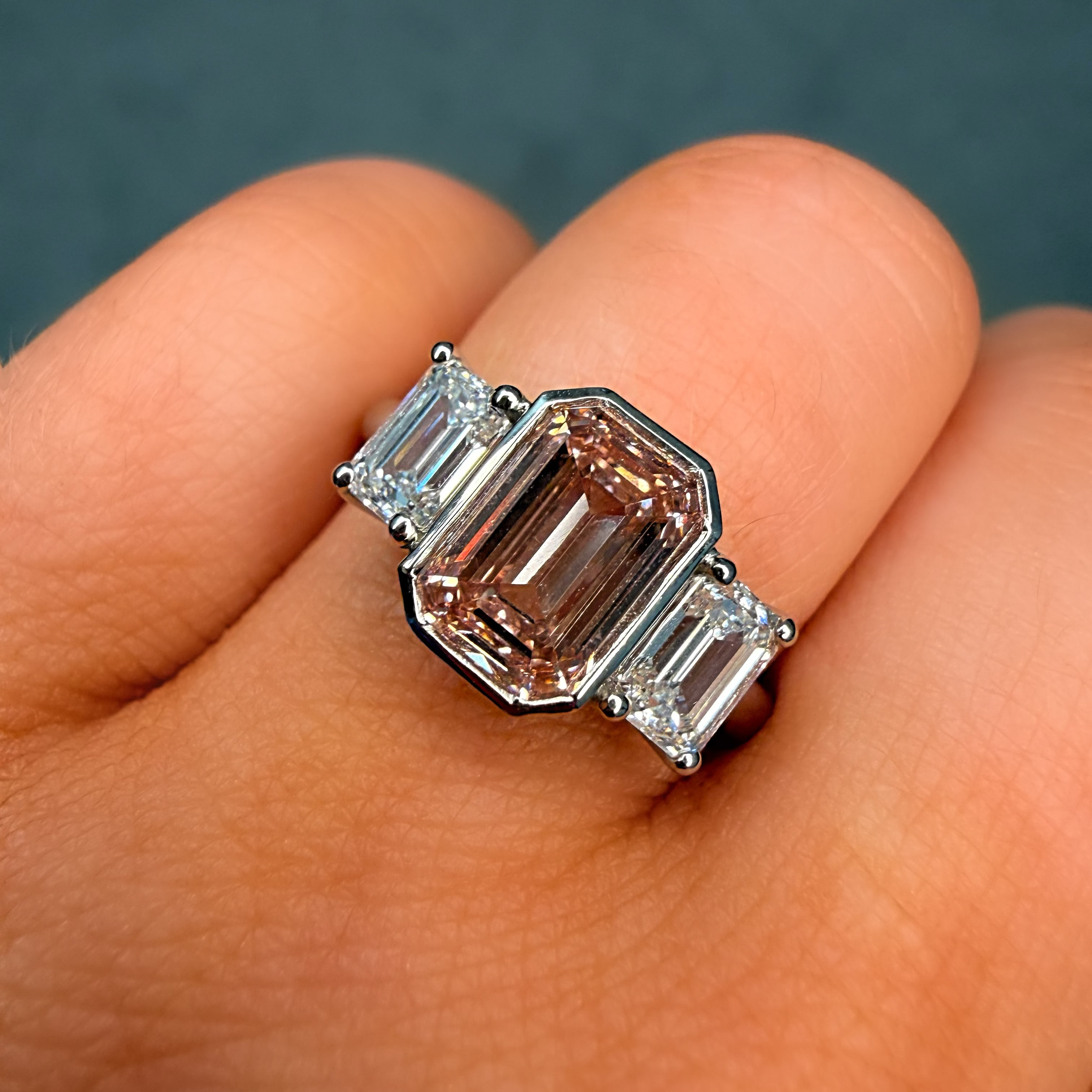 Ring with a pink gemstone and emerald-cut diamonds on a finger against a dark background