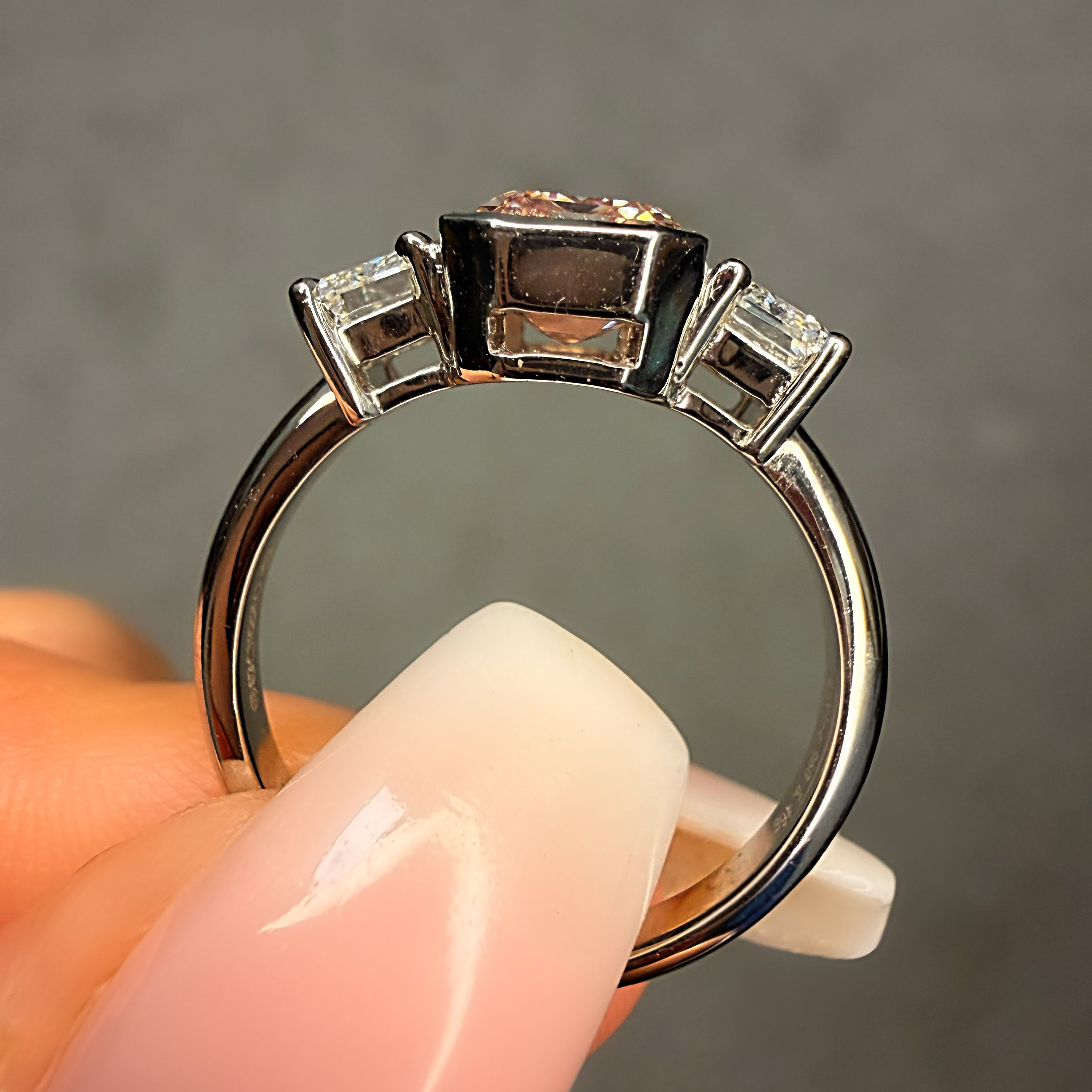 Silver ring with a central black gemstone and two smaller clear stones held by a hand against a gray background