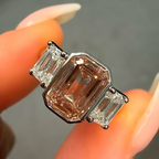 Diamond ring with a pink center stone held between fingers against a neutral background