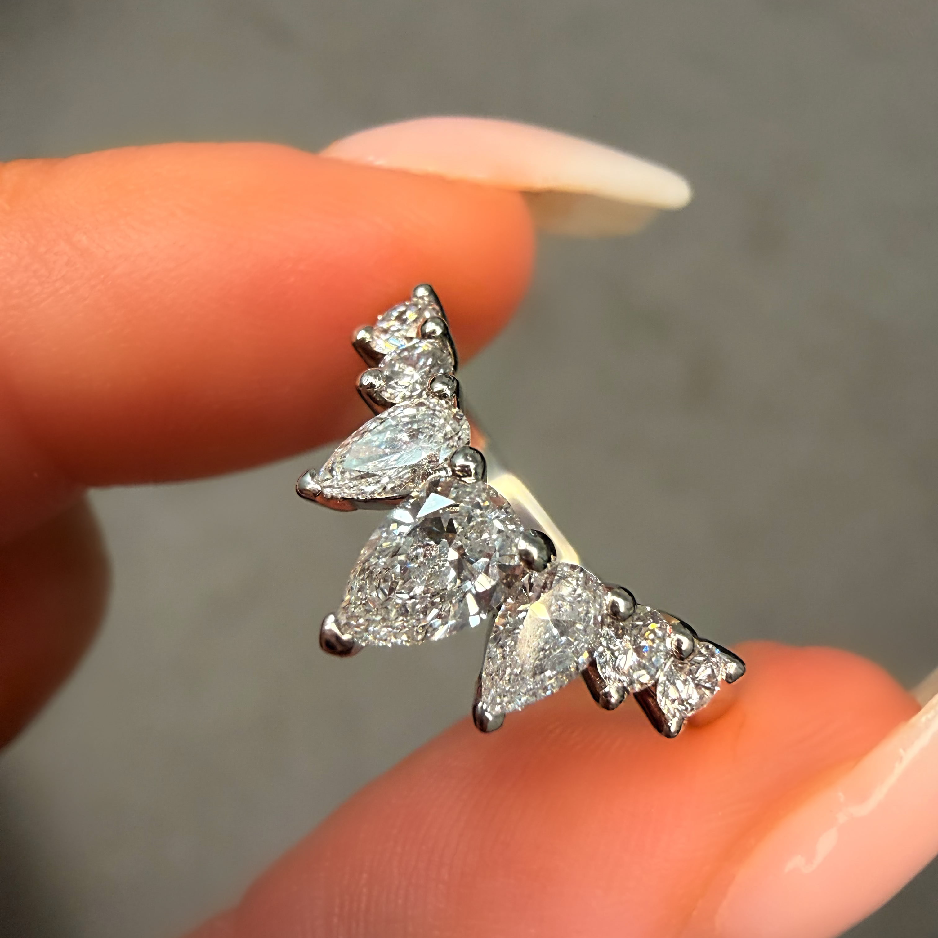 Diamond earrings held between fingers against a neutral background