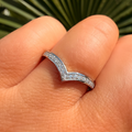 Silver ring with small diamonds on a finger against a green leafy background