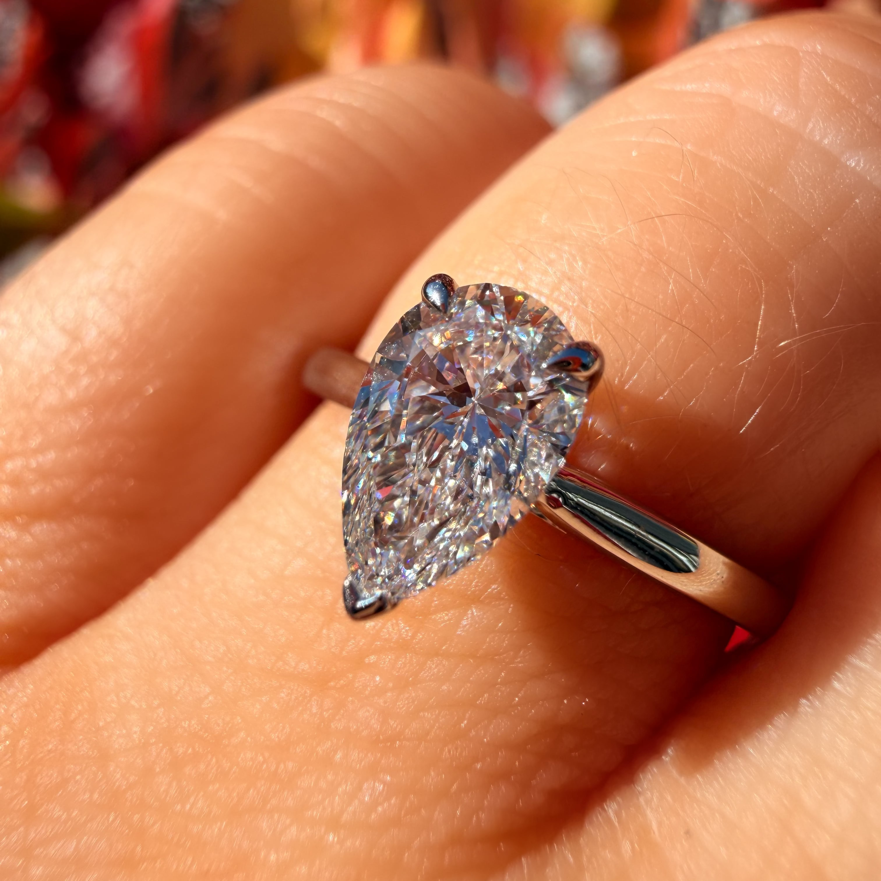 A pear-cut diamond ring set in a silver-colored band, worn on a finger. The diamond is held in four prongs and features a brilliant cut with sparkling facets.