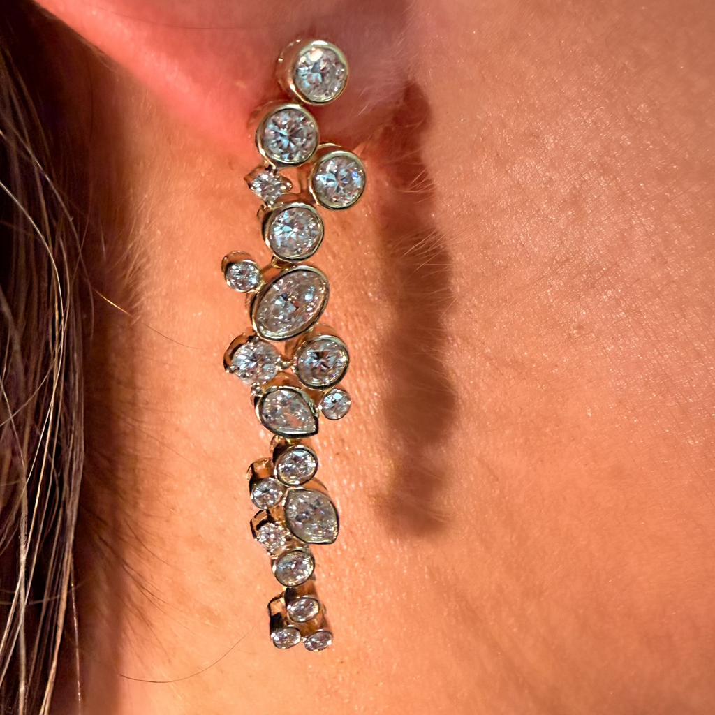 A close-up of a gold-toned drop earring with multiple clear round and oval gemstones worn on a person's ear.