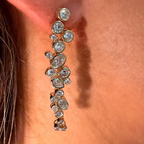 A close-up of a gold-toned drop earring with multiple clear round and oval gemstones worn on a person's ear.