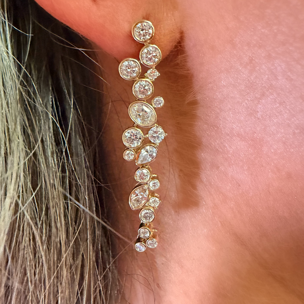 A close-up of a gold dangle earring with multiple clear round-cut gemstones worn on a person's ear.
