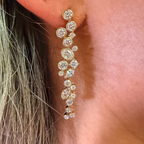 A close-up of a gold dangle earring with multiple clear round-cut gemstones worn on a person's ear.