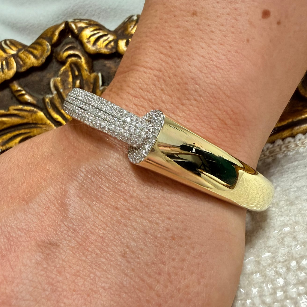 A close-up of a gold and diamond cuff bracelet worn on a person's wrist, featuring a polished gold band and a diamond-encrusted knotted section.